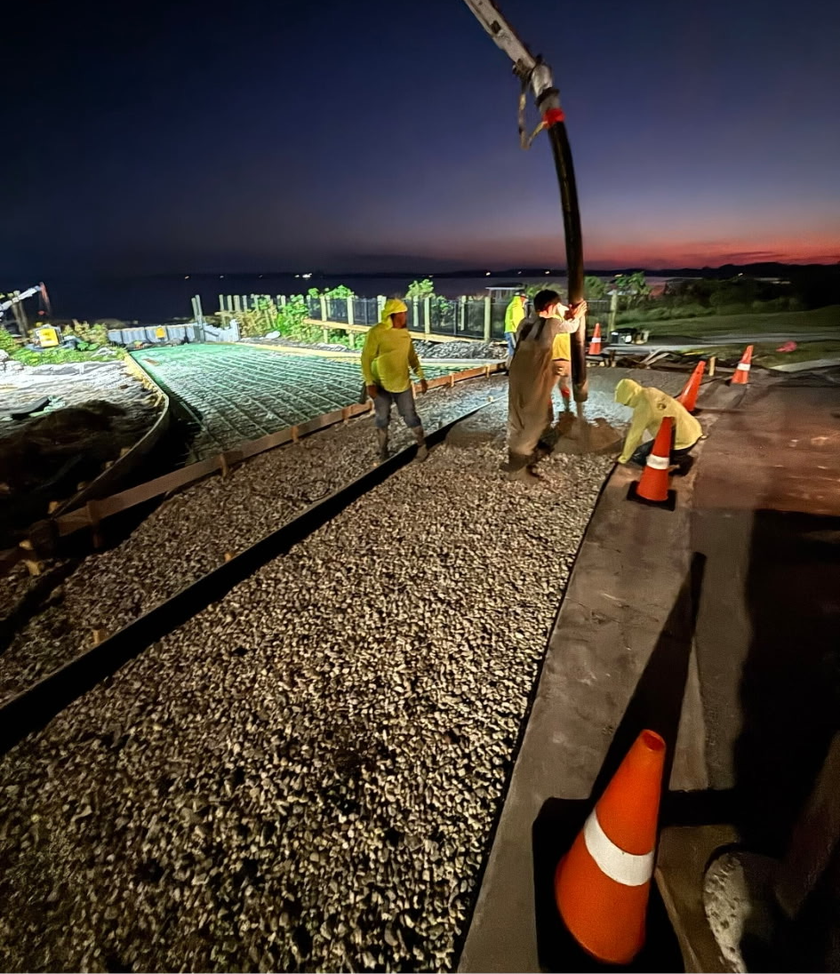 Crew placing concrete off a pump truck hose at dusk on a boat ramp